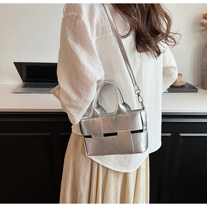 Silver metallic woven handbag with detachable shoulder strap shown on a desk