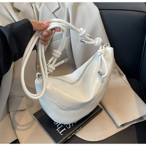 Detail of white glossy dumpling bag showing unique knotted shoulder strap and metal hardware