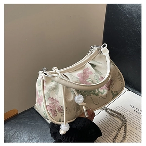 Detail of embroidered floral patterns and bead tassel on an off-white half-moon bag