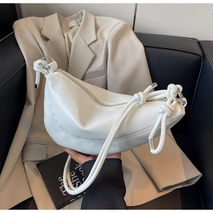 Detail of white half-moon shoulder bag featuring knot strap and silver ring hardware