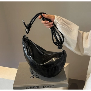 Detail of black glossy hobo bag featuring knotted shoulder strap and silver hardware
