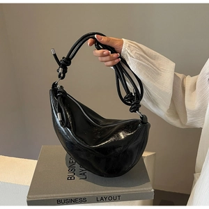 Detail of black glossy crinkled leather crescent bag with knot strap and silver hardware
