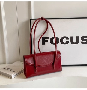 Detail of red patent leather shoulder bag with glossy finish and metal buckles