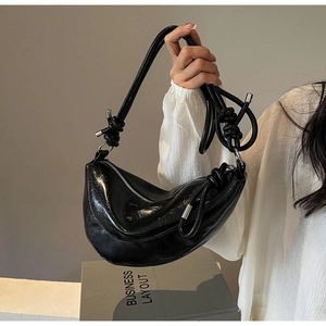 Detail of black glossy crescent bag featuring a unique knotted shoulder strap and silver hardware