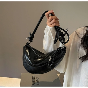 Detail of black glossy crescent bag featuring unique knotted strap and silver hardware