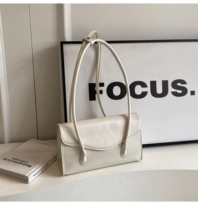 Detail of cream white leather baguette bag with curved flap and long shoulder strap