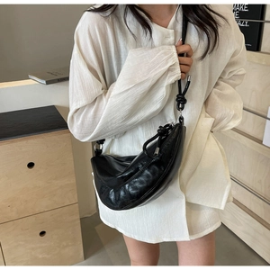 Detail of black croissant bag with knot handle and wrinkled leather texture on white shirt