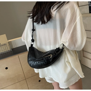 Detail view of black glossy patent leather crescent bag with adjustable knotted shoulder strap