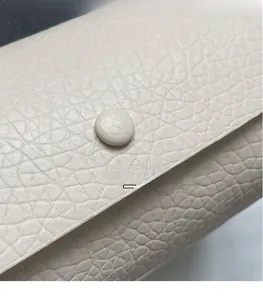 Detail of beige lychee grain leather handbag featuring a round leather-covered buckle