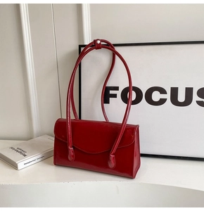 Close-up of a glossy red patent leather underarm bag with sleek metal buckles