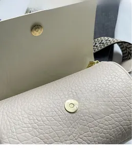 Detailed close-up of golden magnetic clasp on beige lychee leather cylindrical crossbody bag