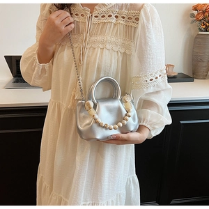 Sac nuage plissé argenté avec perles et chaîne en métal sur un bureau moderne