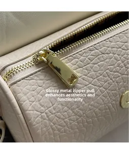Close-up of polished gold hardware zipper and lychee grain leather on beige barrel bag