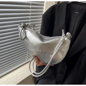 Detail of silver metallic crescent bag featuring crinkled texture and knot strap accents