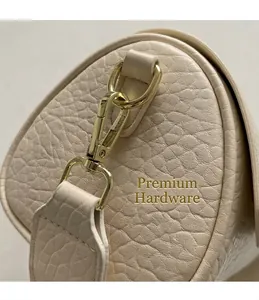 Macro shot of gold metal hardware and litchi grain leather texture on off-white cylindrical bag