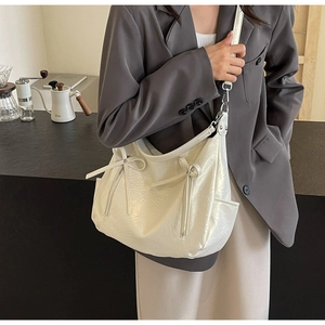 Detail view of a white glossy tote bag with bow accent and metallic hardware on model
