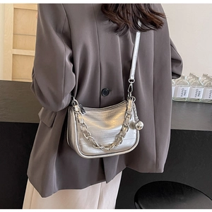 Détail du sac à main argenté métallisé avec chaîne épaisse et breloque boule sur modèle
