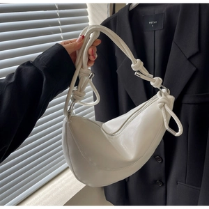 Close-up of a white half-moon bag featuring a knotted strap detail and silver metal hardware