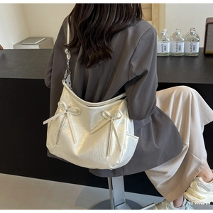 Detail of white hobo bag with bow accents and glossy pleated texture on wide shoulder strap