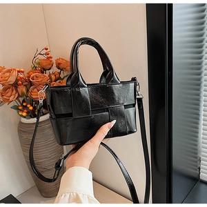 Detail of black woven leather mini tote bag with crossbody strap and rounded top handle