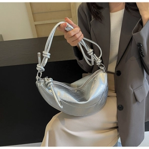 Detail of silver metallic dumpling bag with knotted handle held by a model in casual chic suit