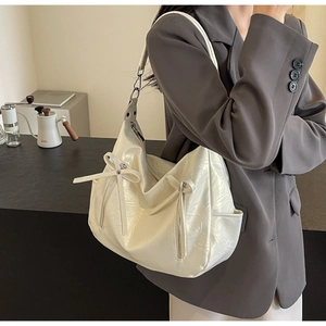Detail of white pleated leather tote bag featuring a bow tie and metal zipper detail