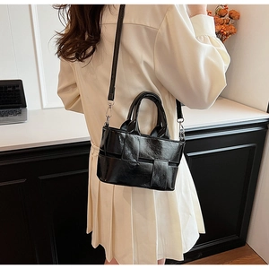 Detail of black woven leather tote bag featuring glossy finish and adjustable shoulder strap