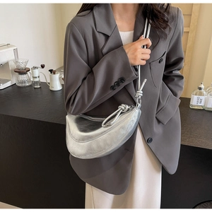 Silver metallic dumpling bag with knotted shoulder strap worn by a model in a cafe