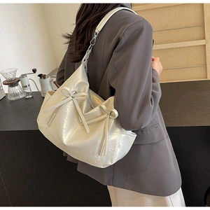 Detail of off-white pleated tote bag with bow accent and zippers in a cafe setting