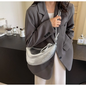 Close-up of a silver crescent handbag with glossy pleated texture and knotted strap detail