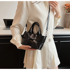 Close-up of woven black glossy leather handbag with crossbody strap and metal buckle