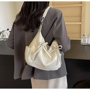 Detail of white pearlescent crossbody bag with bows and ruffles worn by model in cafe