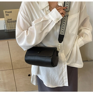 Close-up of black cylinder crossbody bag with geometric pattern wide strap on model