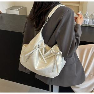 Detail of off-white lychee texture leather bag with elegant bow accents and metal hardware