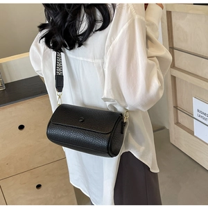 Detail view of black cylinder crossbody bag with geometric woven strap on model