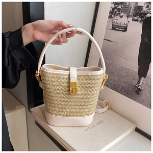Detail of hand-woven straw bucket bag with white leather trim and gold hardware clasp