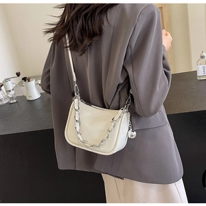 Détail d'un sac bandoulière blanc à motif crocodile avec chaîne argentée sur blazer