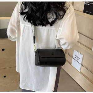 Close-up of black lychee leather cylinder bag with geometric jacquard wide shoulder strap