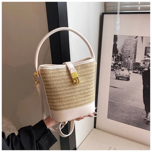 Detail of hand-woven straw bucket bag featuring cream leather trim and gold twist-lock