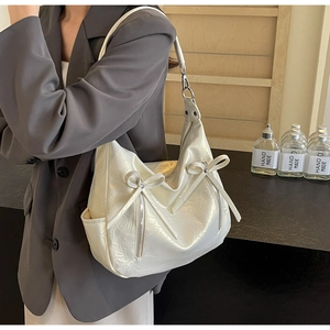 Detail of cream hobo bag with ribbon bows, silver hardware and side pocket on shoulder