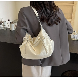 Close-up of a beige bucket bag with bow detail and glossy wrinkled texture