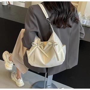 Detail of cream hobo bucket bag with bow accents on model wearing a grey blazer