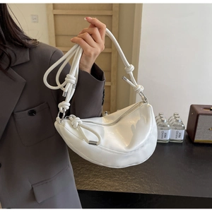 Detail of white glossy crescent bag featuring unique knot decoration and silver hardware