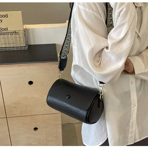 Detail of black cylindrical crossbody bag with lychee texture and wide geometric strap