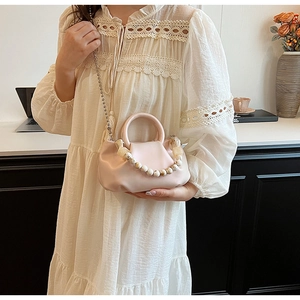 Détail du sac nuage plissé rose avec poignée en perles et chaîne dorée sur robe en dentelle
