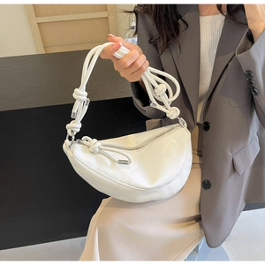 Detail of white glossy crescent bag with knotted strap and silver hardware on model