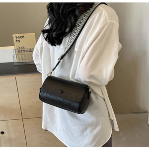 Detail of black cylindrical bucket bag with lychee texture and geometric wide strap