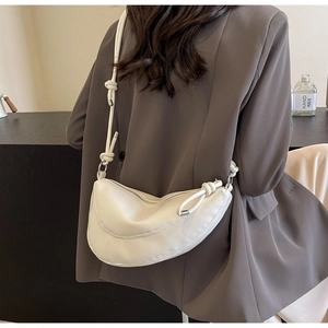 Close-up of minimalist white dumpling bag with unique knotted strap on woman's shoulder