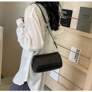 Detail of black textured cylinder crossbody bag with a wide geometric woven strap