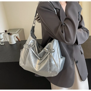 Detail of silver metallic hobo bag featuring bow decorations and side zipper on a model